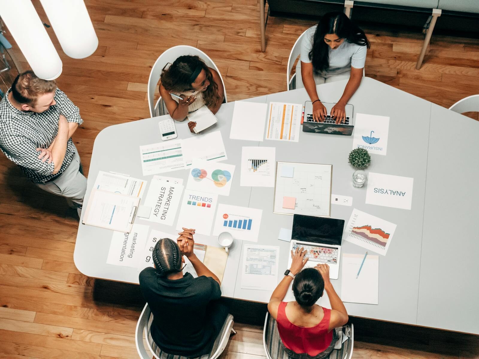 Aerial view of a collaborative meeting with four people around a table, examining marketing strategies and data analysis documents.